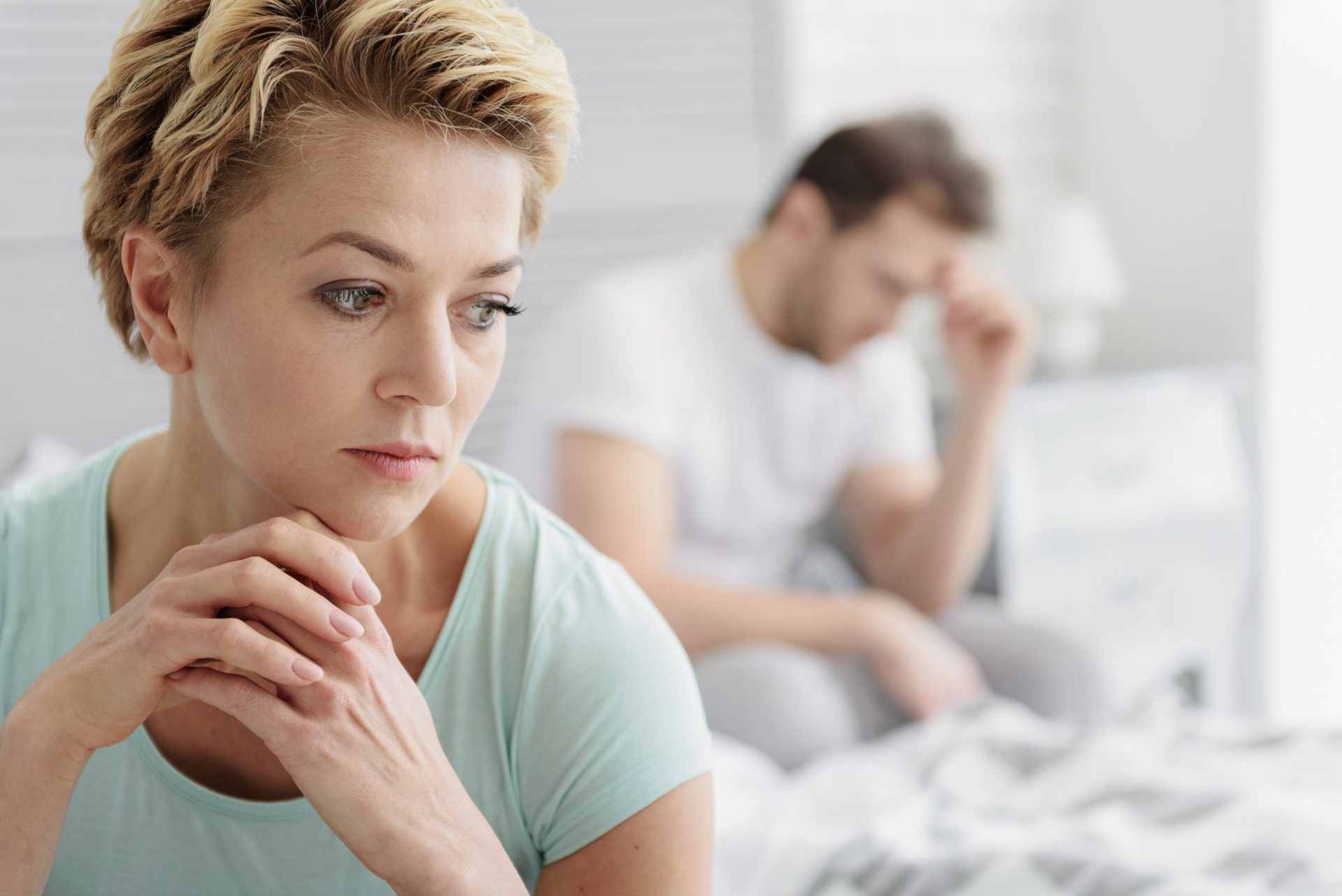 Married couple experiencing crisis in relationship Portrait of pensive middle-aged woman thinking about her marriage with sadness. Her husband is sitting on bed