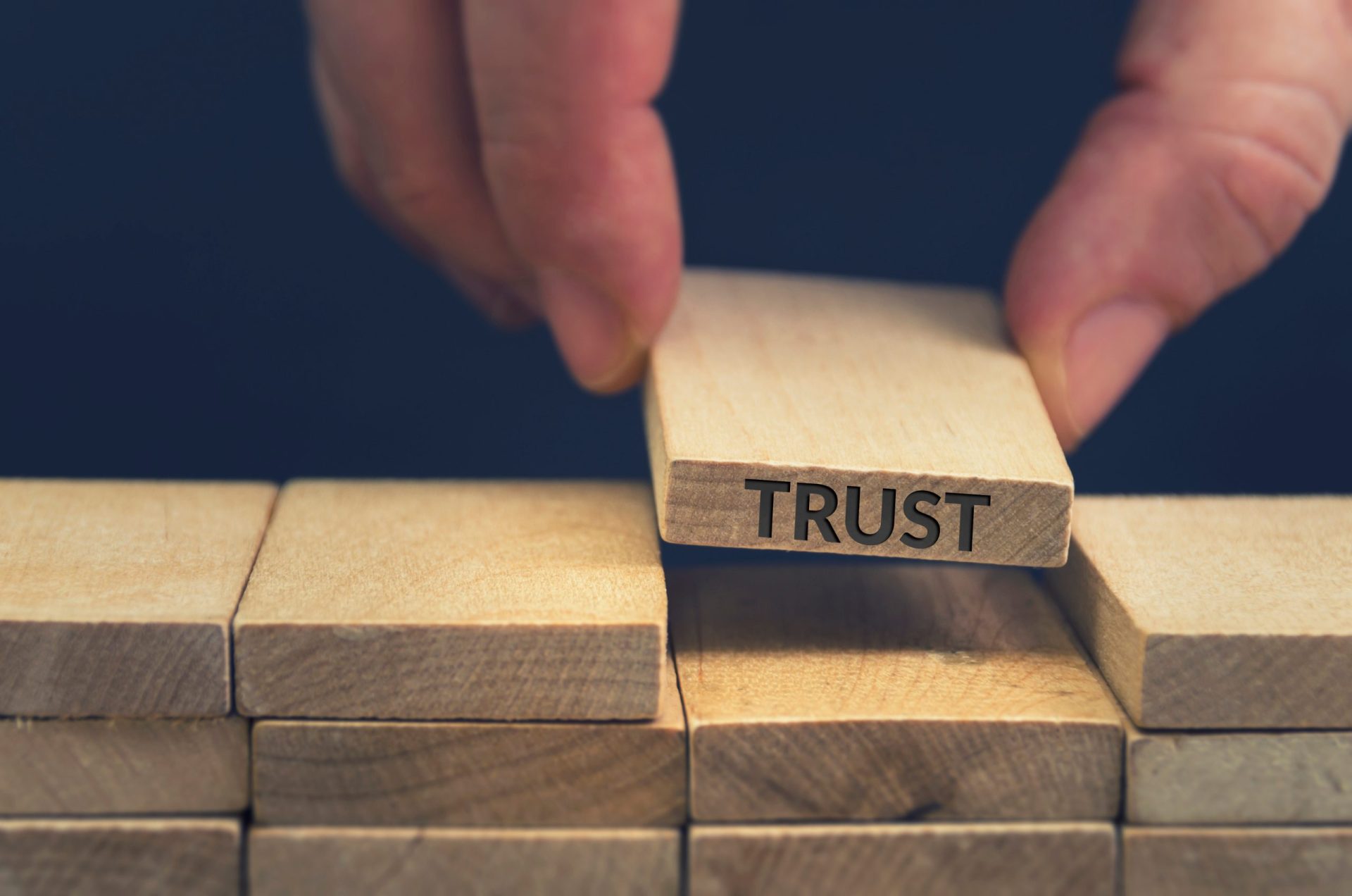 Person holding wooden block that says trust, placing it within a stack of other wooden blocks