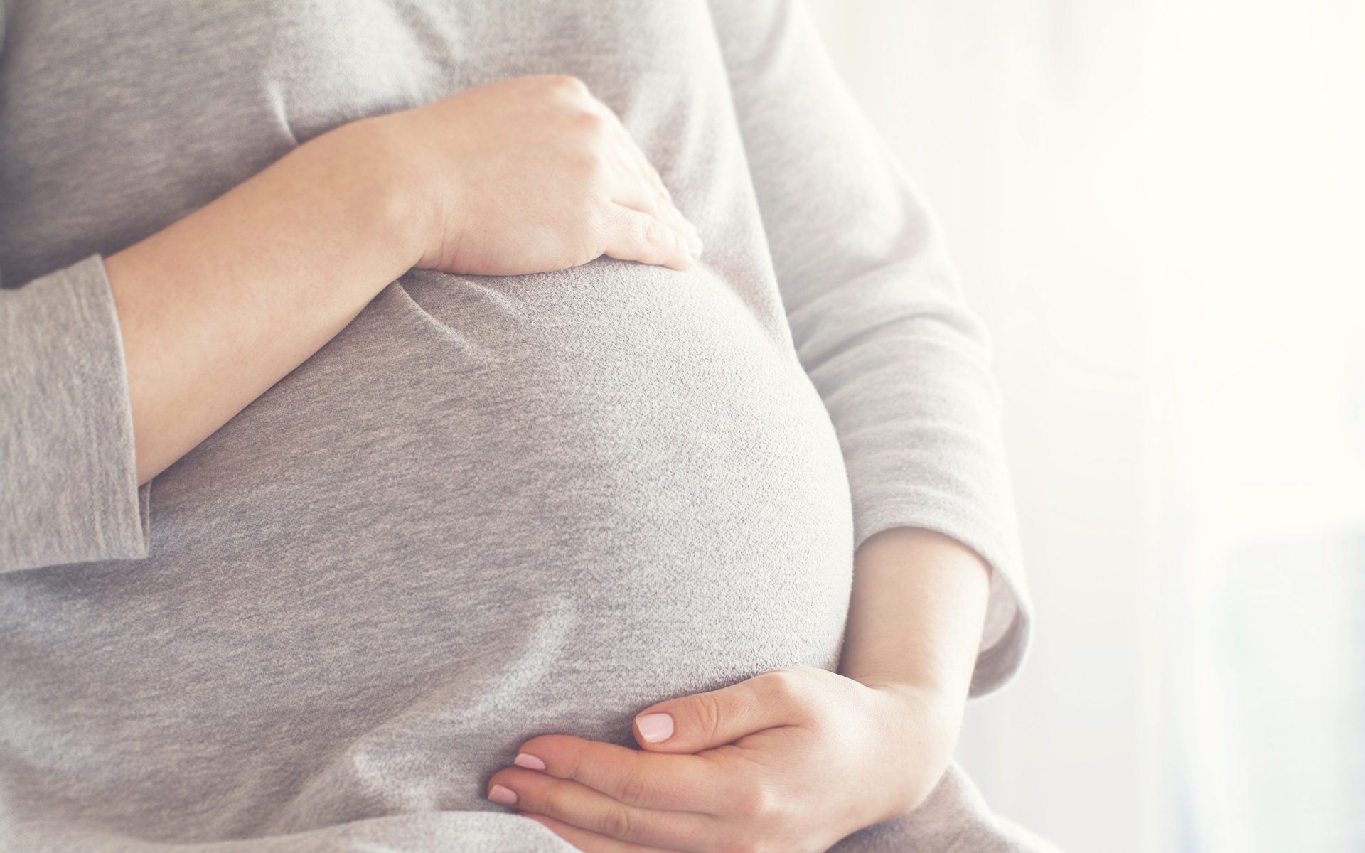 pregnancy Up close photo of a pregnant belly, person wearing grey shirt holding stomach
