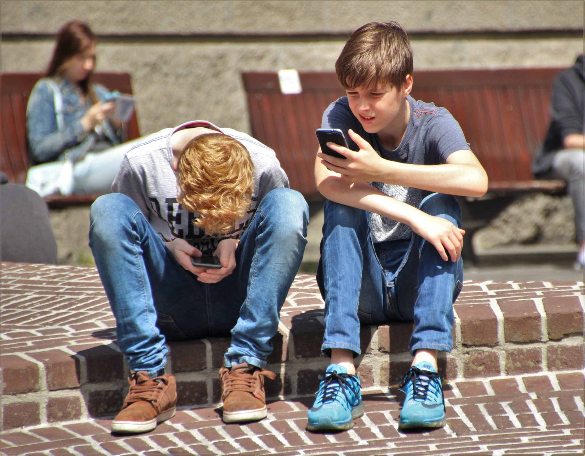Two teens sitting together on their phones