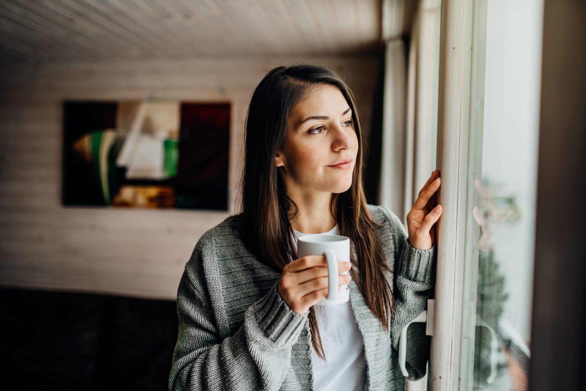 Woman looking contentedly out a window holding a cup of coffee