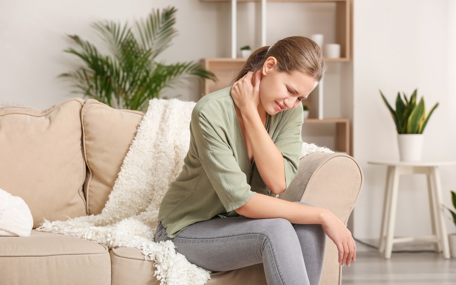 Woman sitting on couch holding neck