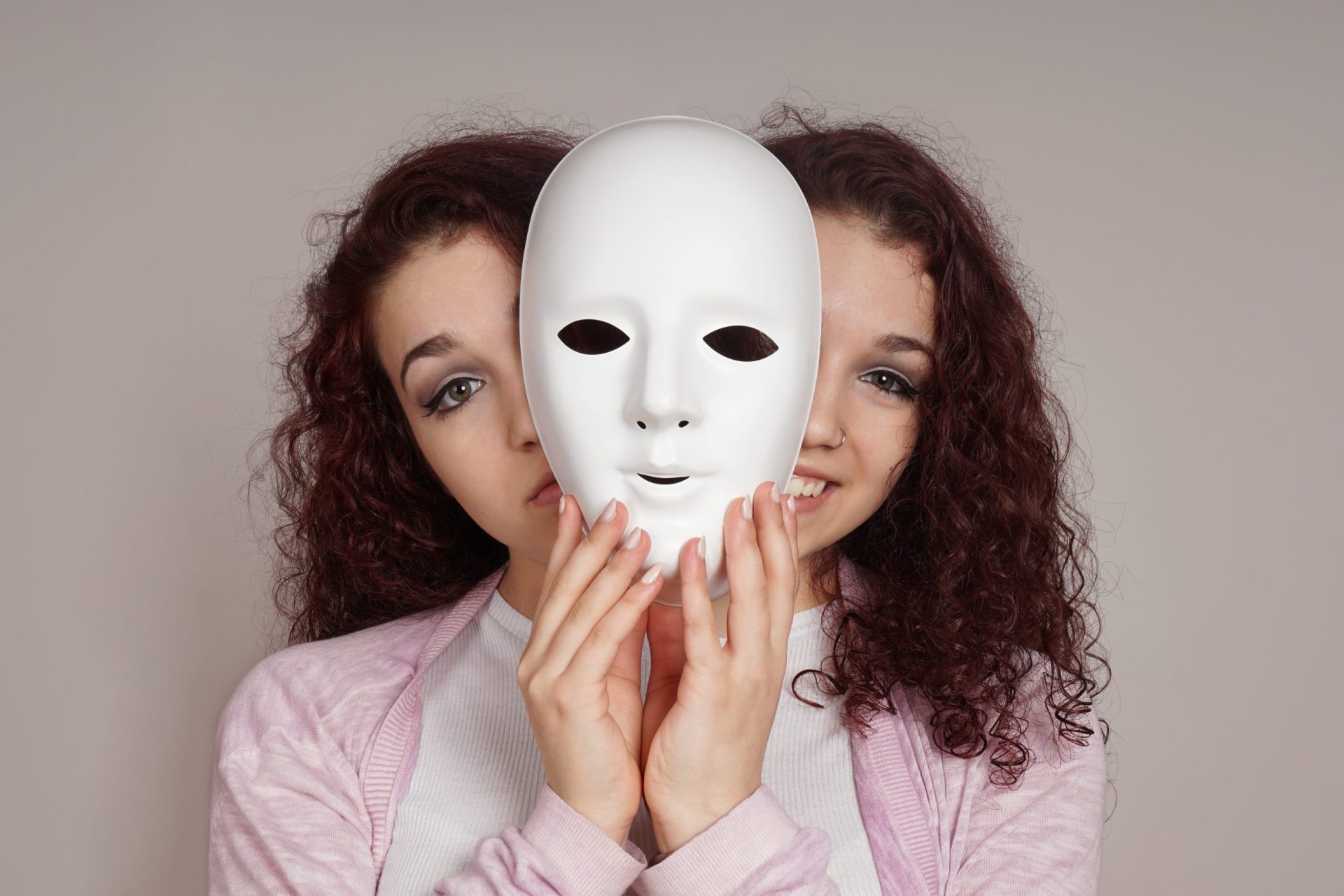 woman holding up a mask peeking out on one side looking sad and on the other looking happy