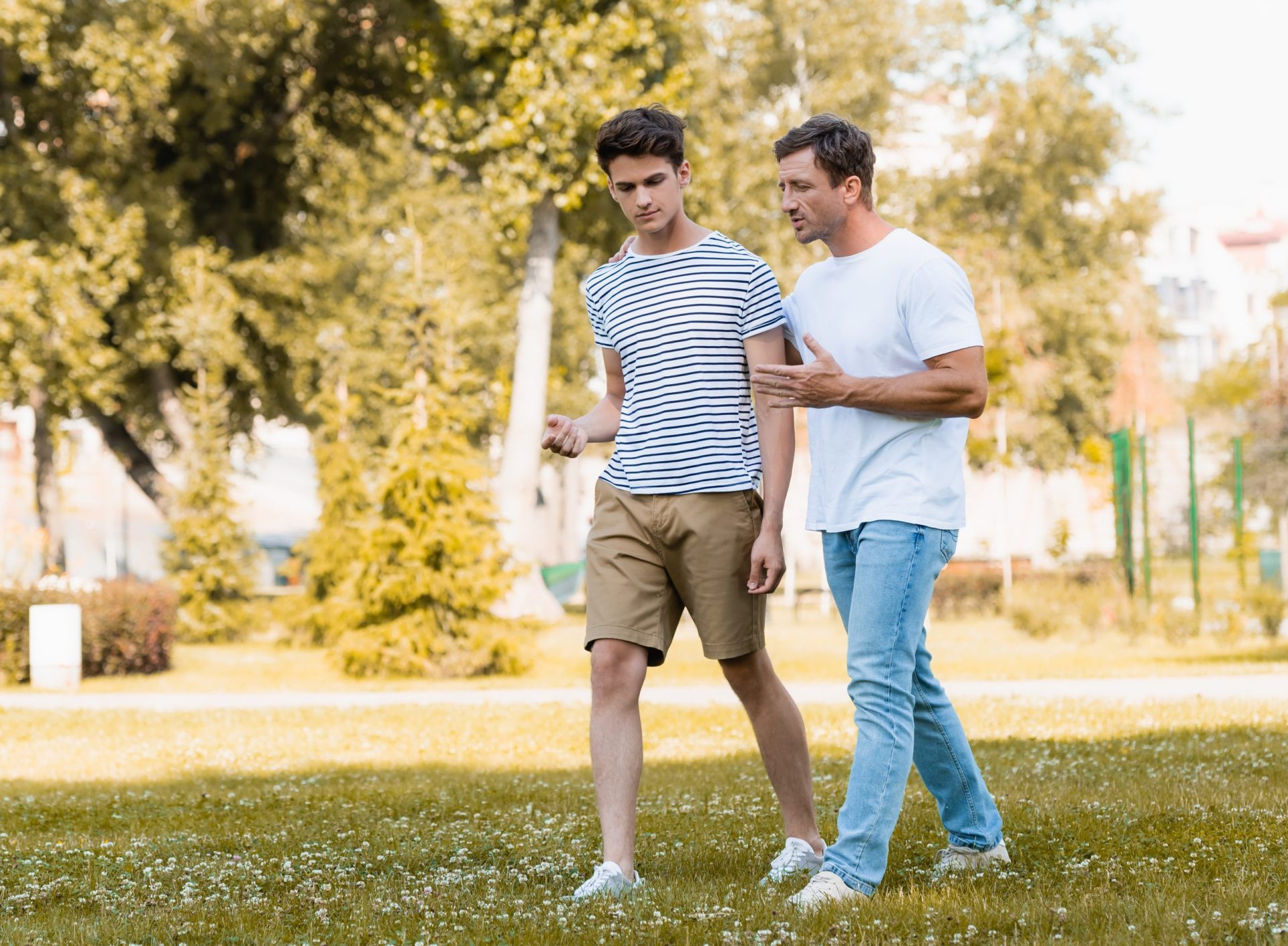 man gesturing while walking and talking with teenager son in park