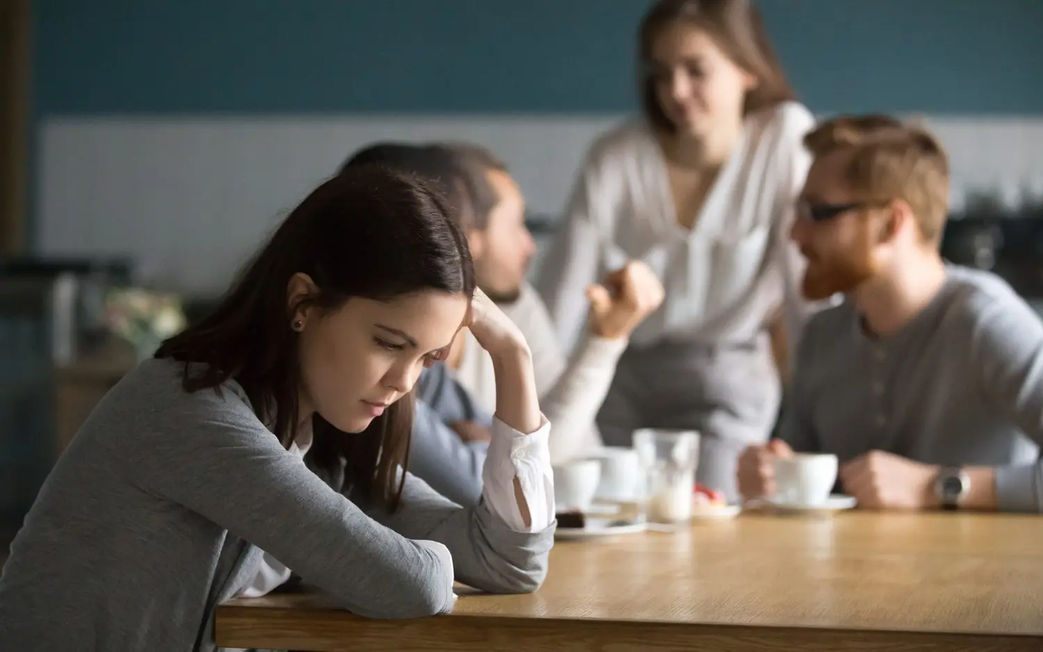 A girl sitting alone with a group of people sitting together out of focus in the background