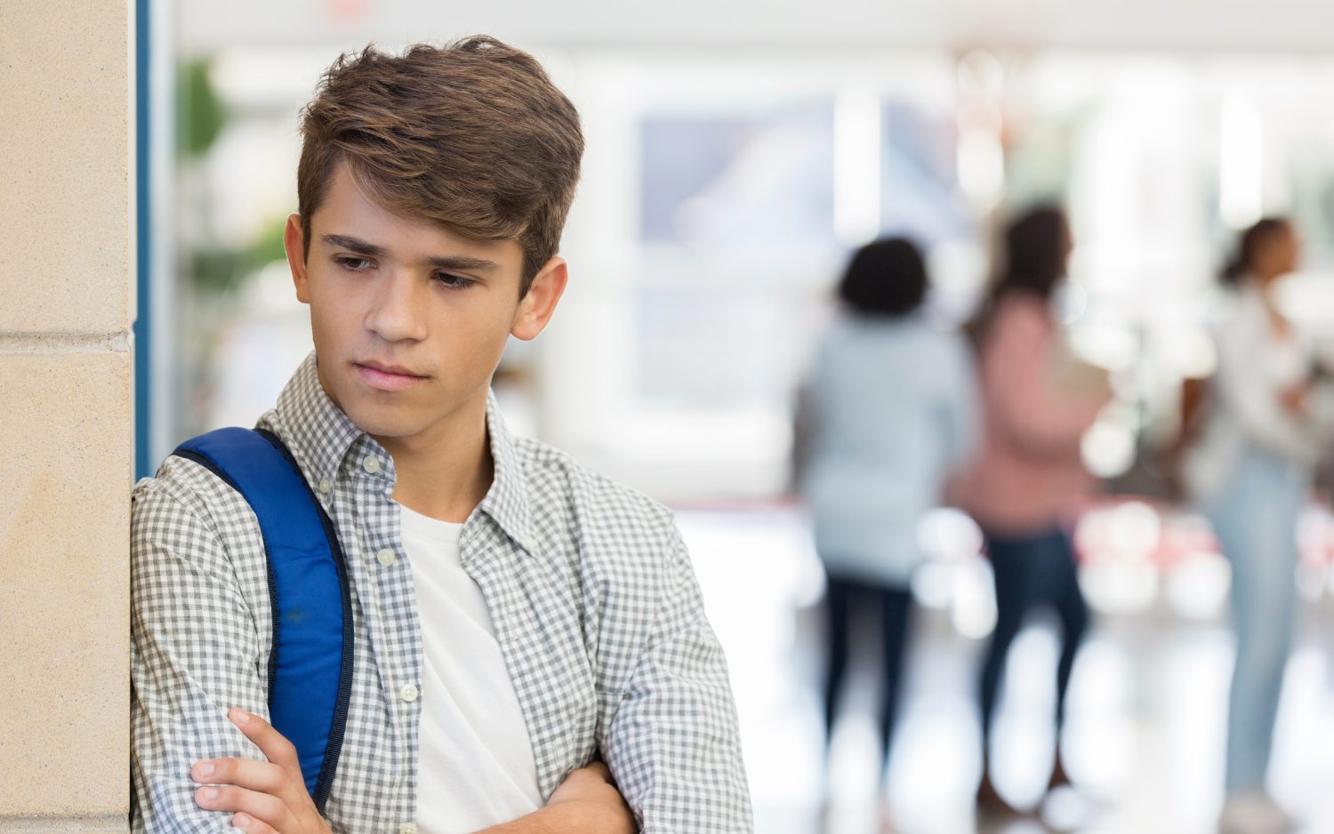 teen boy leaning against a wall at school looking depressed