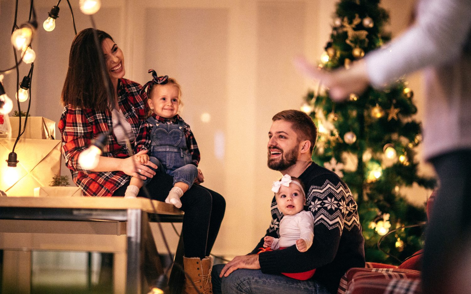 couple sitting together with two small children near a lit tree staying sober during the holidays