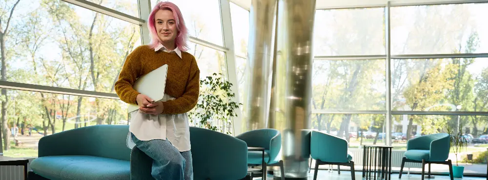 Young female with pink hair standing near sofa in office