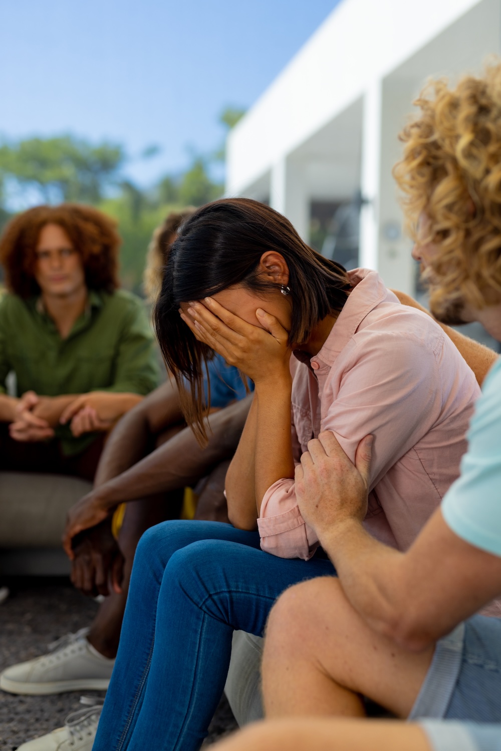 Group of people sitting on sofa, talking and crying in group therapy session. 