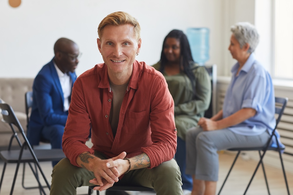 Portrait of smiling tattooed man looking at camera during support group.